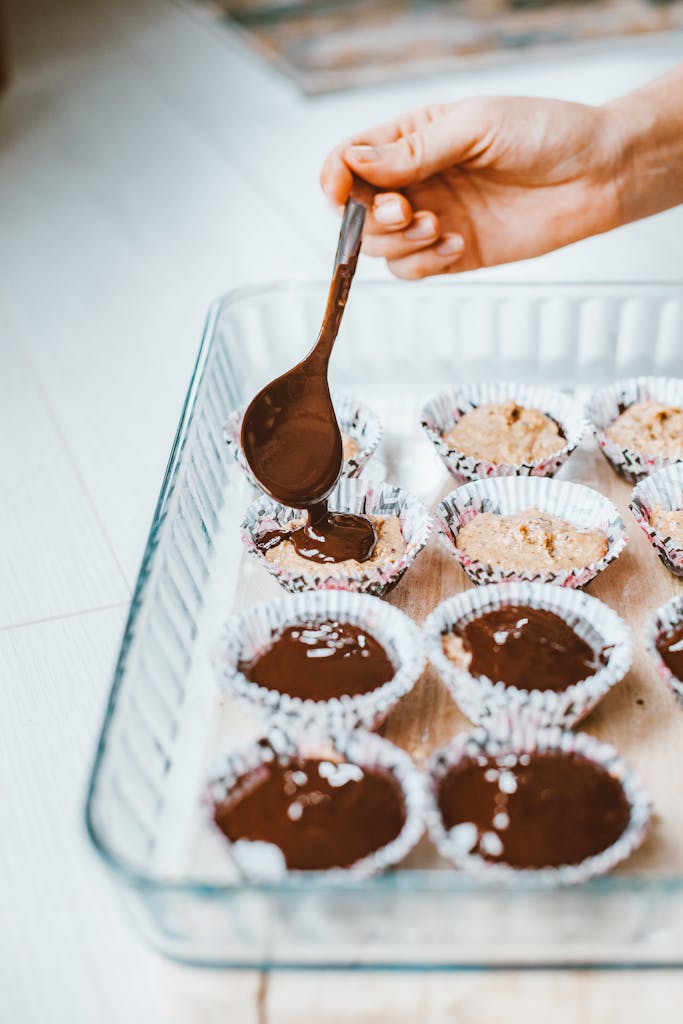 A hand decorating chocolate cupcakes in baking tray showcases culinary skills.