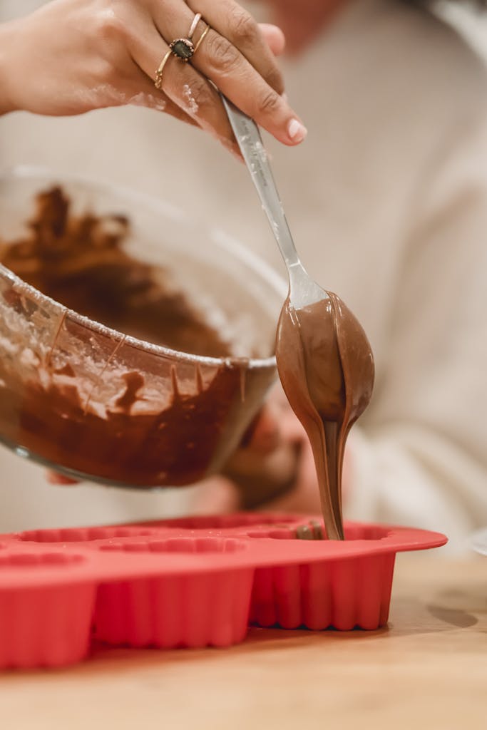 Close-up of a woman pouring chocolate batter into silicone molds in a kitchen.