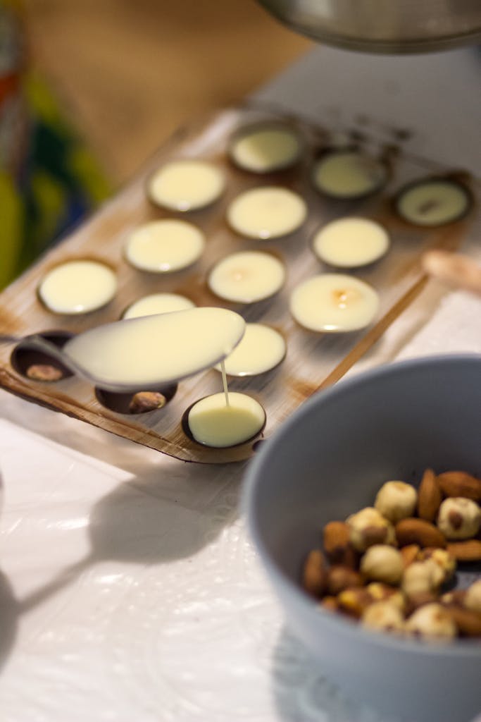 Close-up of white chocolate being poured into molds, surrounded by nuts. Perfect for dessert inspiration.